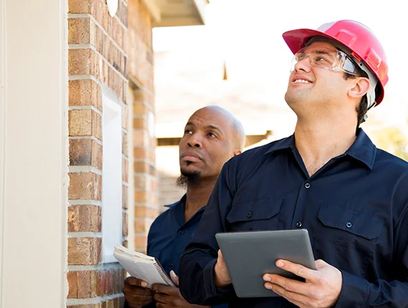 Professional home inspectors discussing property evaluations near a brick structure.